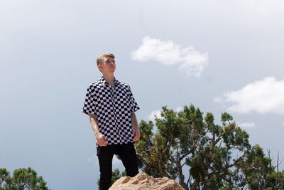 Low angle view of man wearing checked patterned shirt while standing against sky