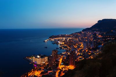 Illuminated city by sea against clear sky at night