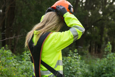 Woman putting on protective helmet to work as a forester in the forest