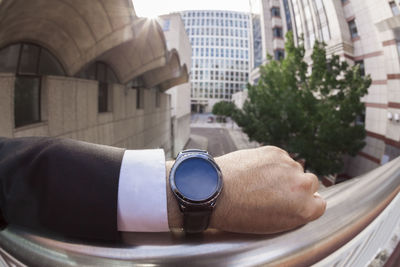 Cropped hand of businessman wearing wristwatch by railing in city