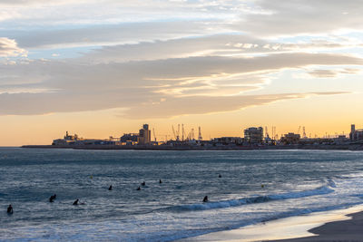 Scenic view of sea by buildings against sky during sunset