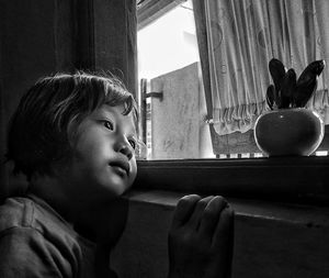 Portrait of boy looking through window at home