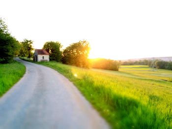 Road amidst field and houses against clear sky