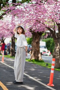 Full length of woman standing by pink flowers on road