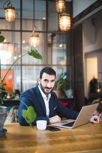 Portrait of confident male professional using laptop while sitting at table in office