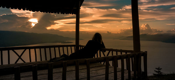 Woman on railing by sea against sky during sunset