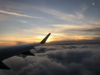 Airplane flying over cloudscape against sky during sunset