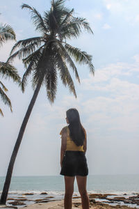 Rear view of woman standing by sea against sky