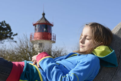 Side view of girl lying outdoors against clear blue sky