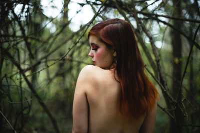 Rear view of topless woman standing in forest