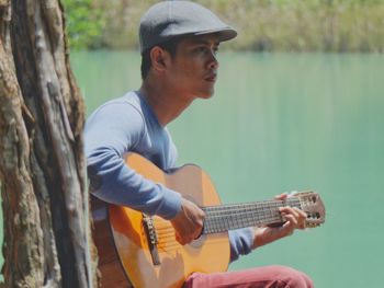 Young man playing guitar by lake