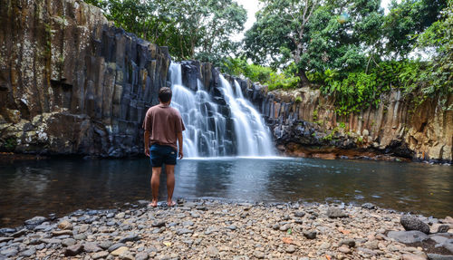 Rear view of man standing against waterfall