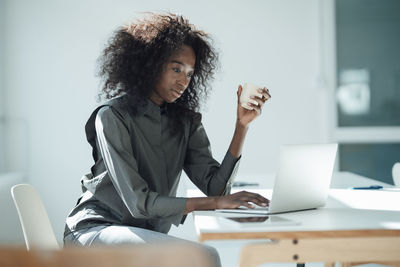 Businesswoman holding coffee cup using laptop at desk in office