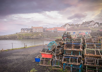 Pile of crab pot on field by river against cloudy sky