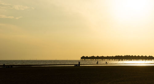 Silhouette people on beach against sky during sunset