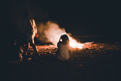 Rear view of woman standing by bonfire at night