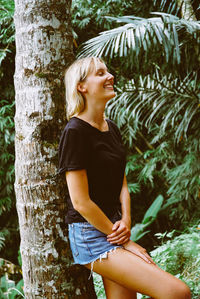 Smiling woman standing against tree trunk
