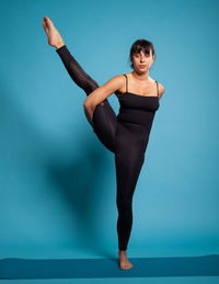 Full length of woman exercising against blue background