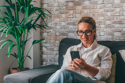Young man using mobile phone while sitting against wall