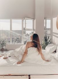 Rear view of young woman sitting on bed at home