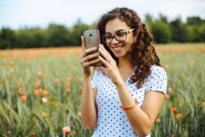 Young woman using phone while standing on field