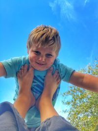Low angle portrait of smiling boy against blue sky