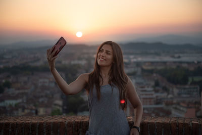 Young woman taking selfie against sky during sunset