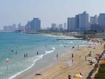 People at beach against sky on sunny day in city