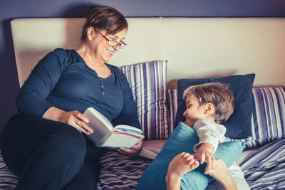 Smiling grandmother reading book for grandson on bed