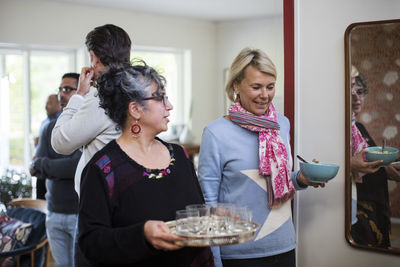 Women holding serving tray and bowl with men standing in background