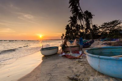 Men fishing at beach against sky during sunset