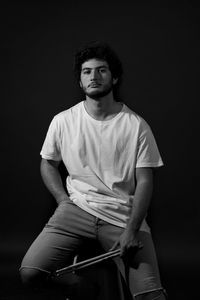 Portrait of young man sitting against black background