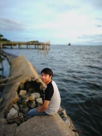 Portrait of young man sitting on broken groyne in sea