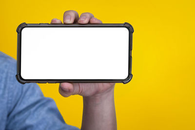 Low section of person holding smart phone against yellow background
