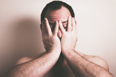 Close-up of shirtless man covering face against wall