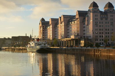 Buildings by river against sky in city