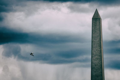 Single flying bird and obelisk in front of stormy rain clouds in glasgow