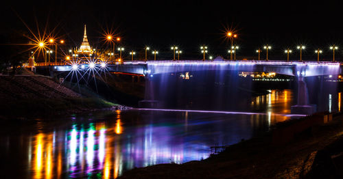 Illuminated bridge over river in city at night