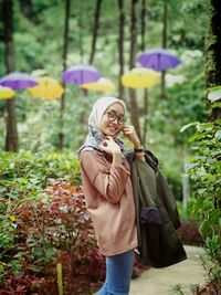 Portrait of young woman standing on footpath amidst plants