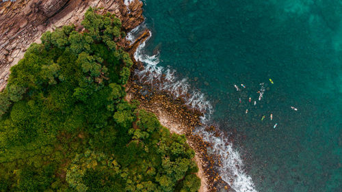 Tropical coast, surfers, ocean and waves crashing against rocks, drone shot, exotic landscape.