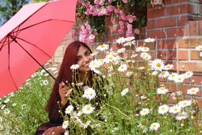 Portrait of woman with umbrella sitting by flowering plants in park