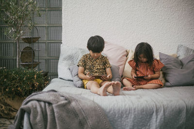 Sister with disability by sibling using smart phones while sitting on sofa at home