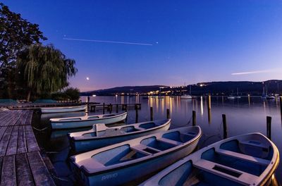 Boats moored in lake against clear blue sky at dusk