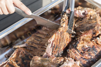 Cropped image of woman chopping grilled rib with knife