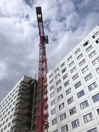 Low angle view of crane by building against sky