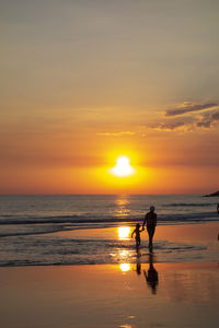 Silhouette people on beach against sky during sunset