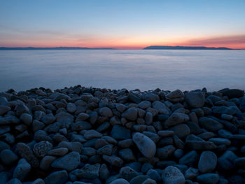 Pebbles on beach against sky during sunset