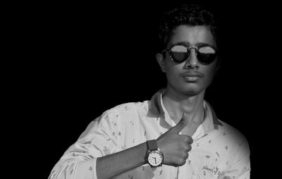 Portrait of young man wearing sunglasses against black background
