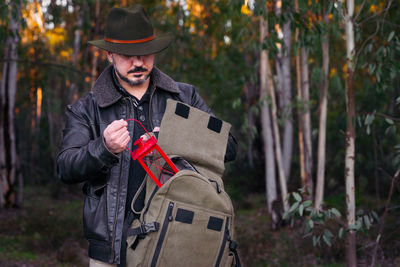 Man removing lantern from bag while standing against trees in forest