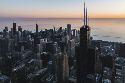 Aerial view of buildings in city against by lake sky during sunset